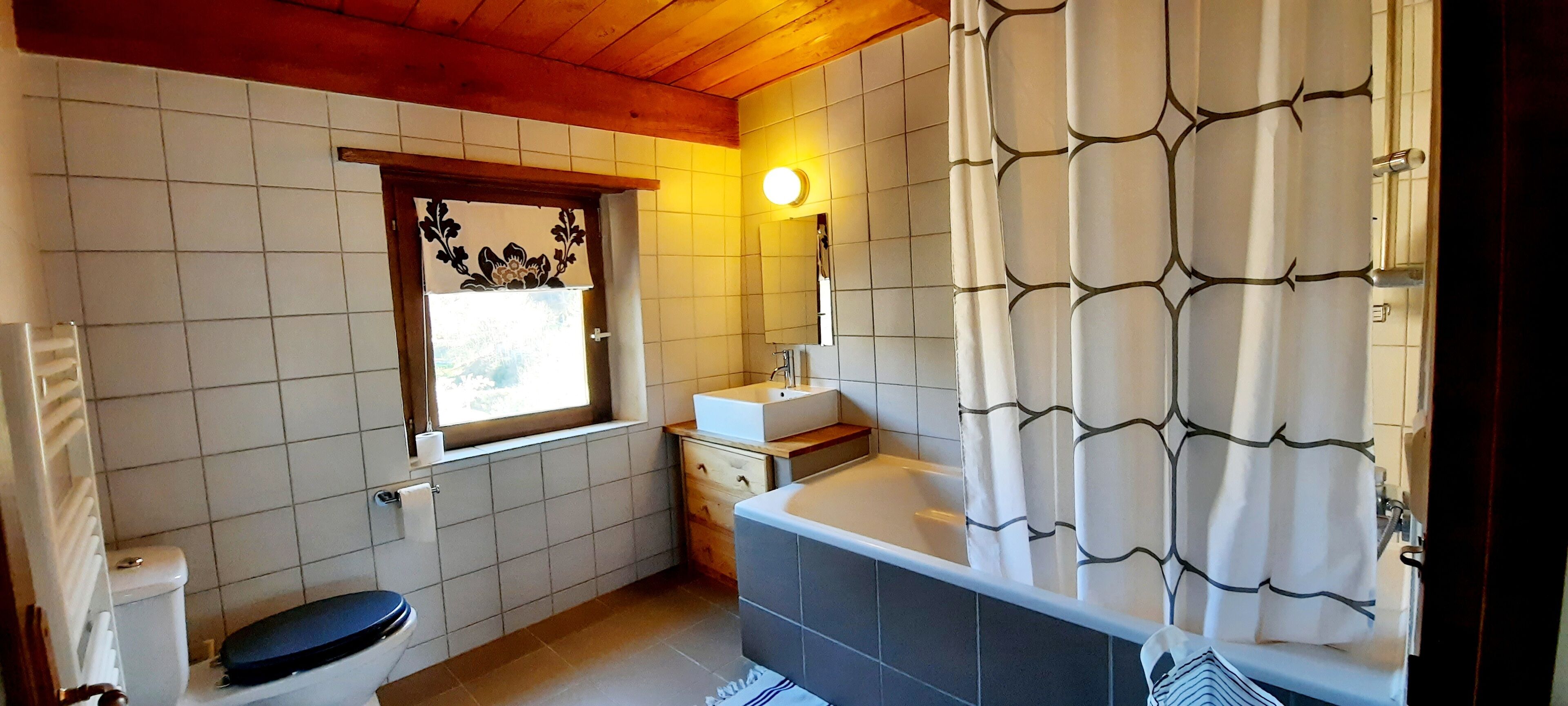 A bathroom with a bathtub, toilet, and window with curtains.