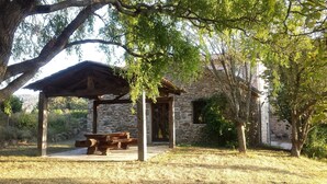 Un edificio in pietra con una pergola in legno e un tavolo da picnic immerso nel verde.