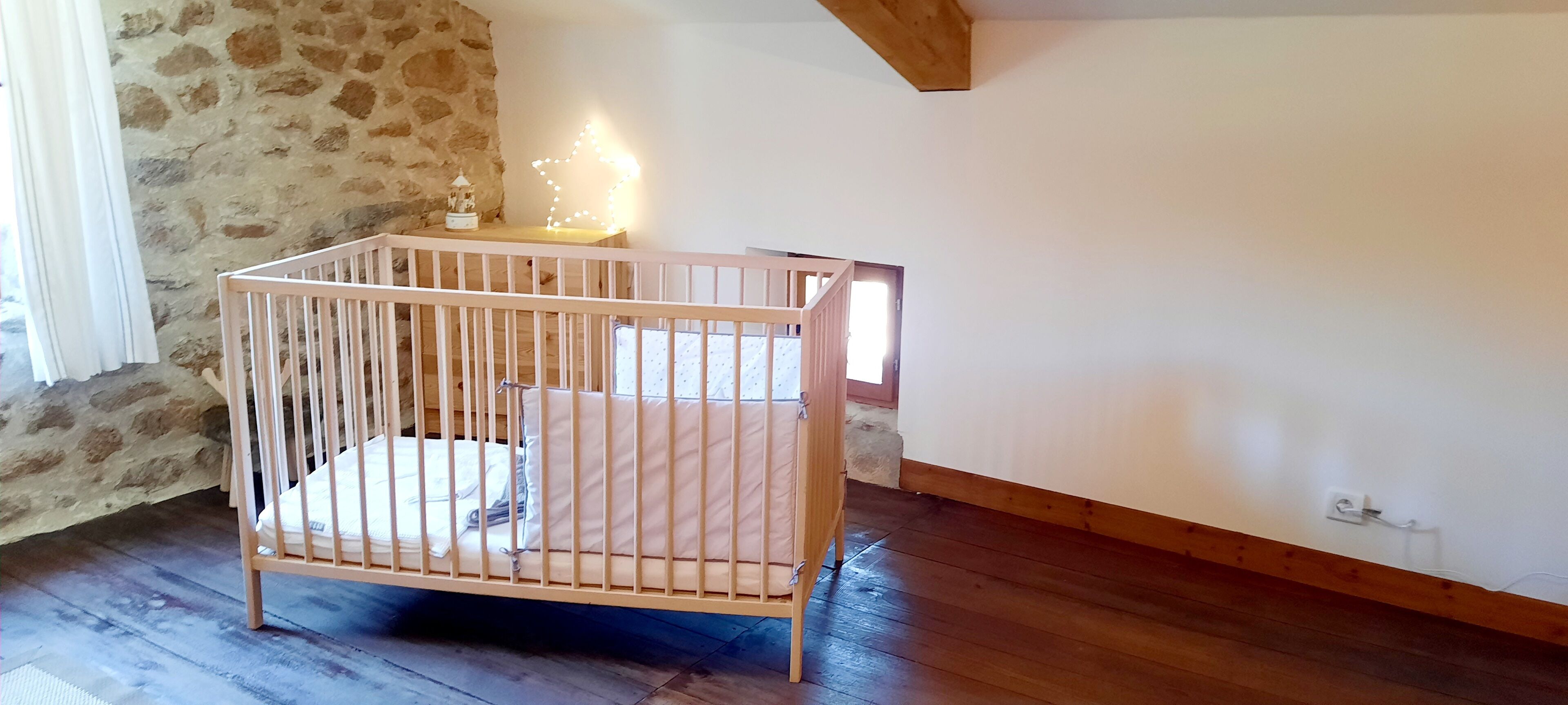 Una cuna de madera en una habitación con paredes de piedra y suelo de madera.