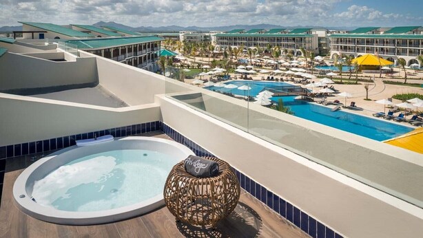 A rooftop pool area with a hot tub, lounge chairs, and a view of a resort complex. - Ocean El Faro - Privilege RoofTop Junior Suite Pool view (Punta Cana)