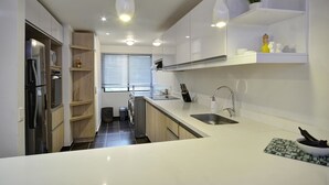 Une cuisine moderne avec des meubles blancs, un évier en acier inoxydable et des luminaires suspendus.