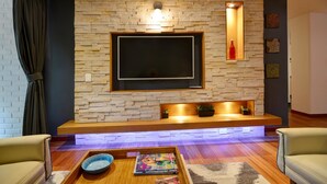 Un salon moderne avec un mur en pierre, un téléviseur à écran plat, un banc en bois et une table basse avec des magazines.