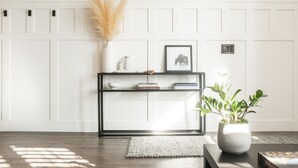 Un salon moderne avec un mur recouvert de panneaux blancs, une console noire agrémentée d’objets décoratifs, une plante en pot et un tableau encadré.