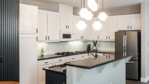 Une cuisine moderne avec des meubles blancs, un îlot central noir, des appareils en acier inoxydable et des suspensions lumineuses à motifs hexagonaux.