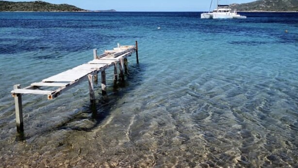 A pier extending into clear blue water with a sailboat in the distance.