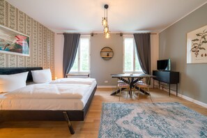 Une chambre à coucher avec un lit, un bureau, une chaise, un téléviseur et une grande fenêtre.