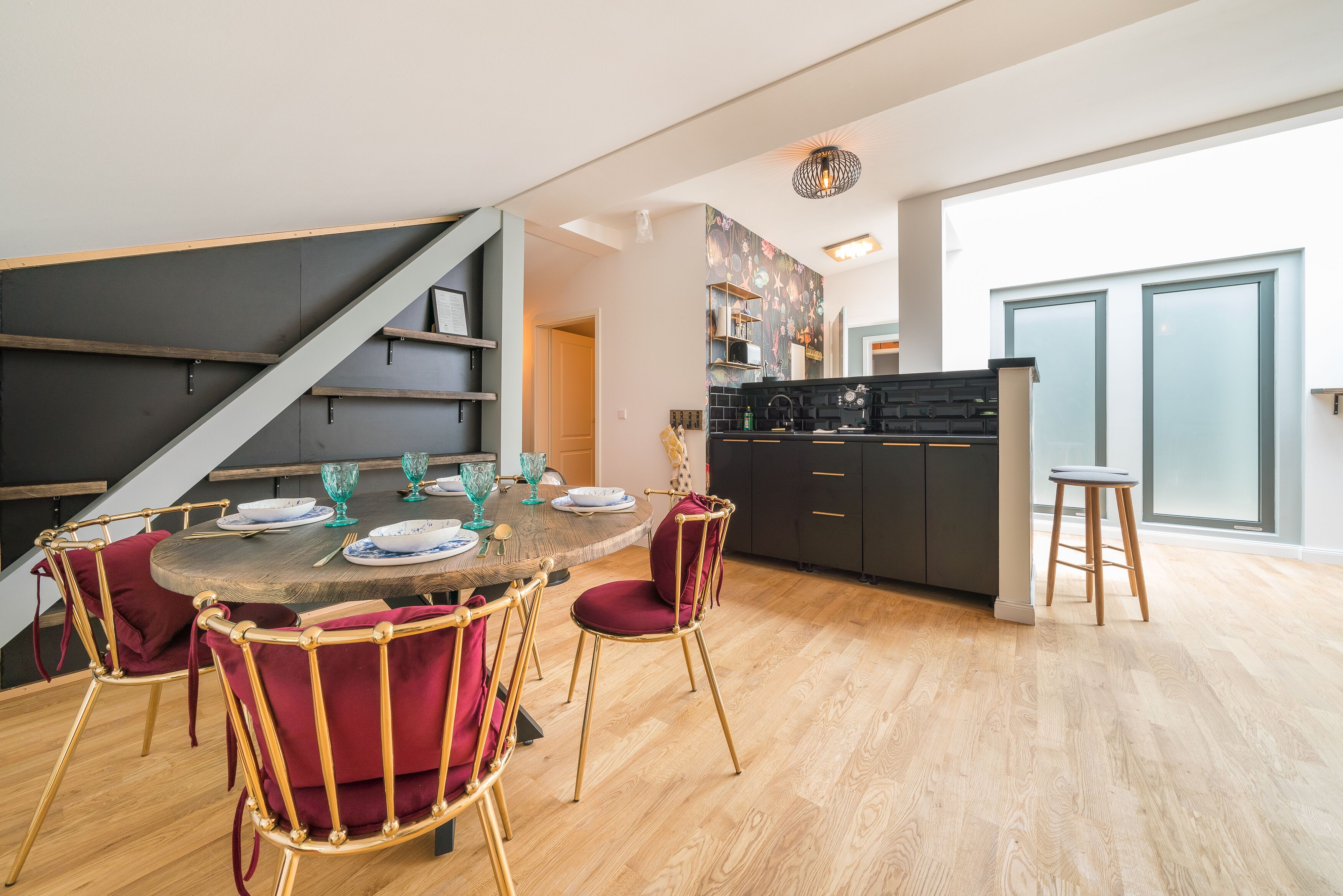 A dining area with a round table, red upholstered chairs, and a kitchen in the background.