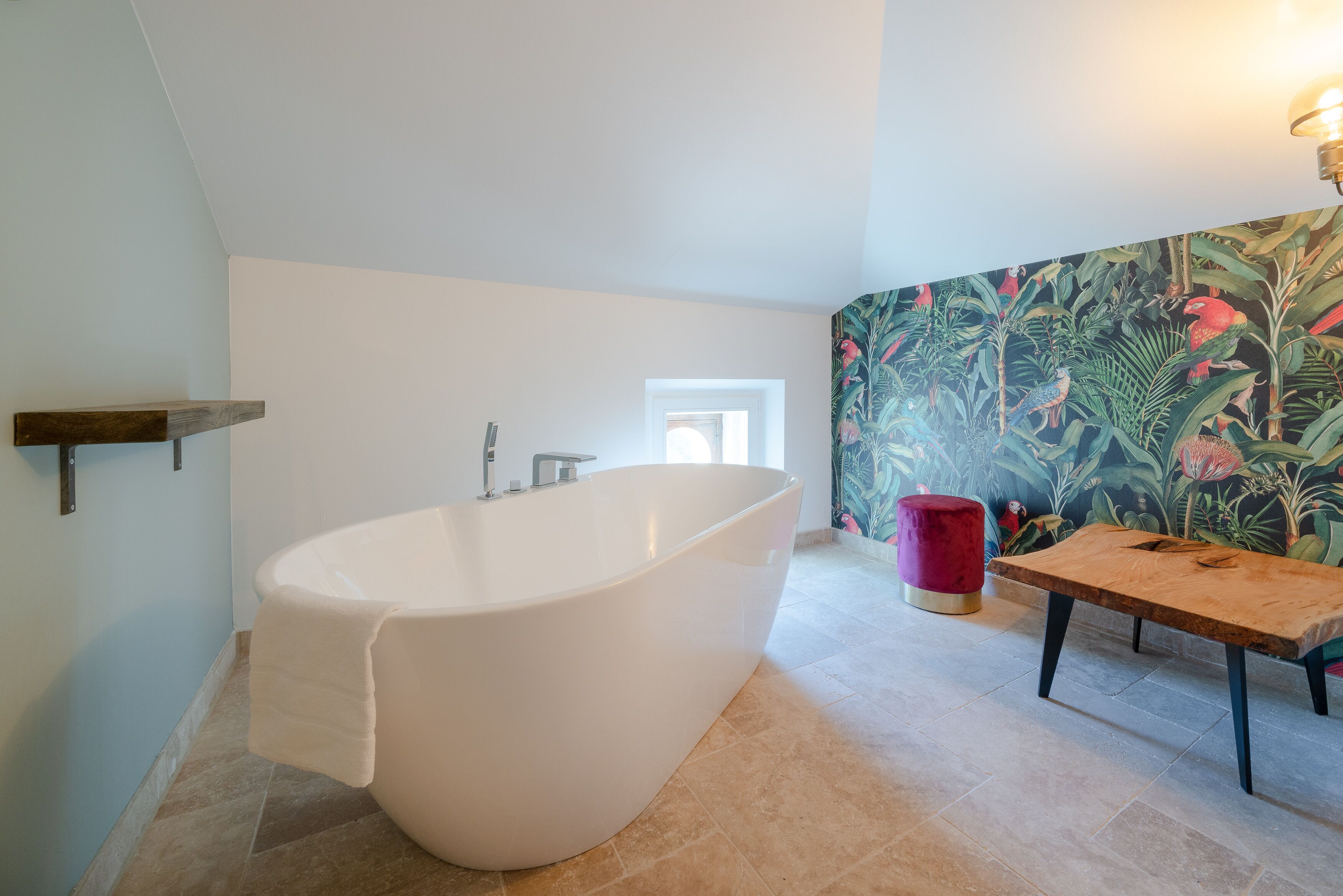 Un bagno moderno con una vasca freestanding, una panca in legno e una carta da parati tropicale dai colori vivaci.