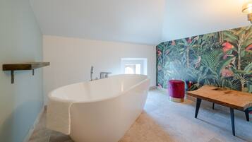 Un bagno moderno con una vasca freestanding, una panca in legno e una carta da parati tropicale dai colori vivaci.