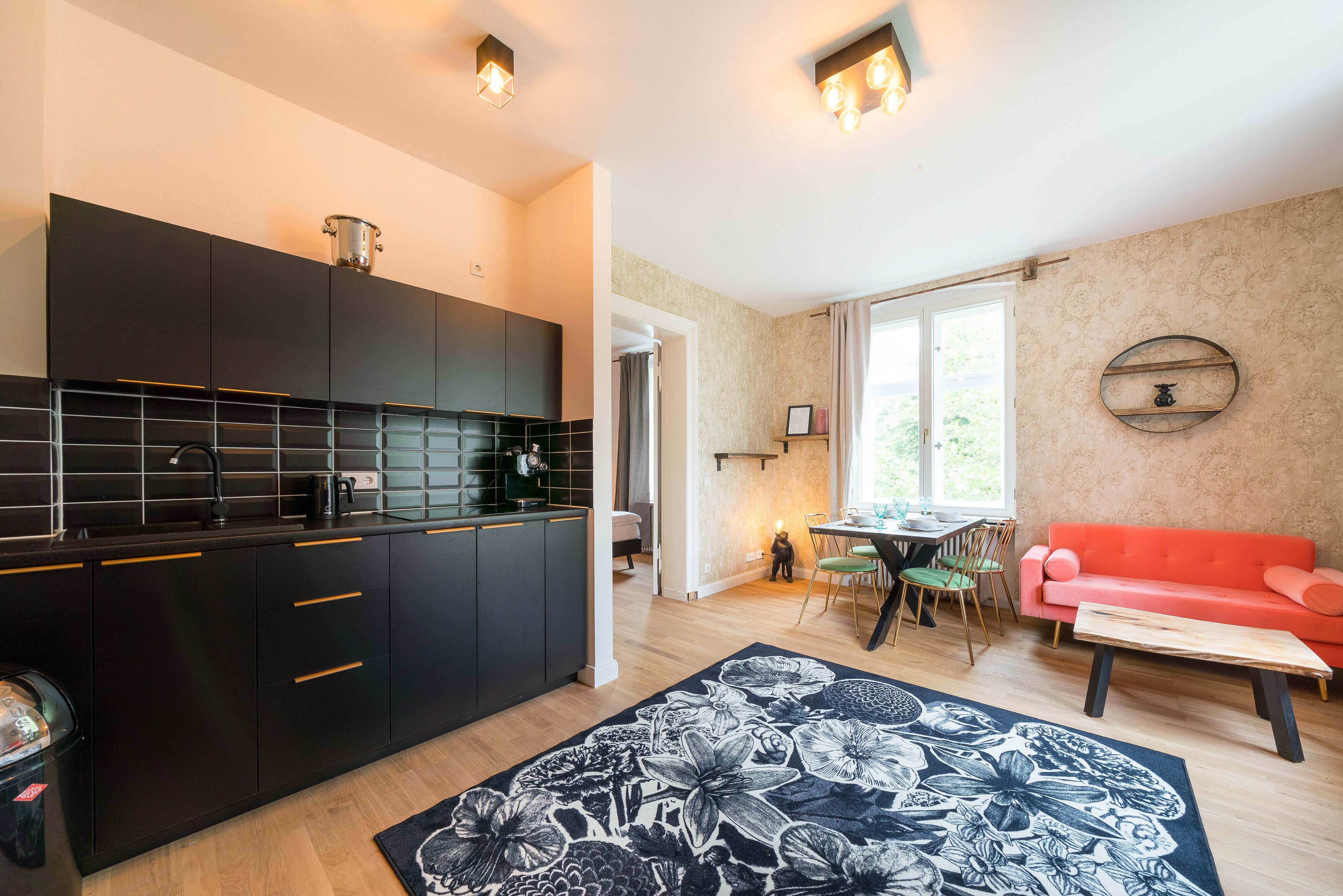 A modern kitchen with black cabinets, a dining area with a red sofa, and a floral rug.