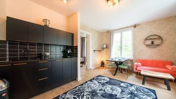 A modern kitchen with black cabinets, a dining area with a red sofa, and a floral rug.