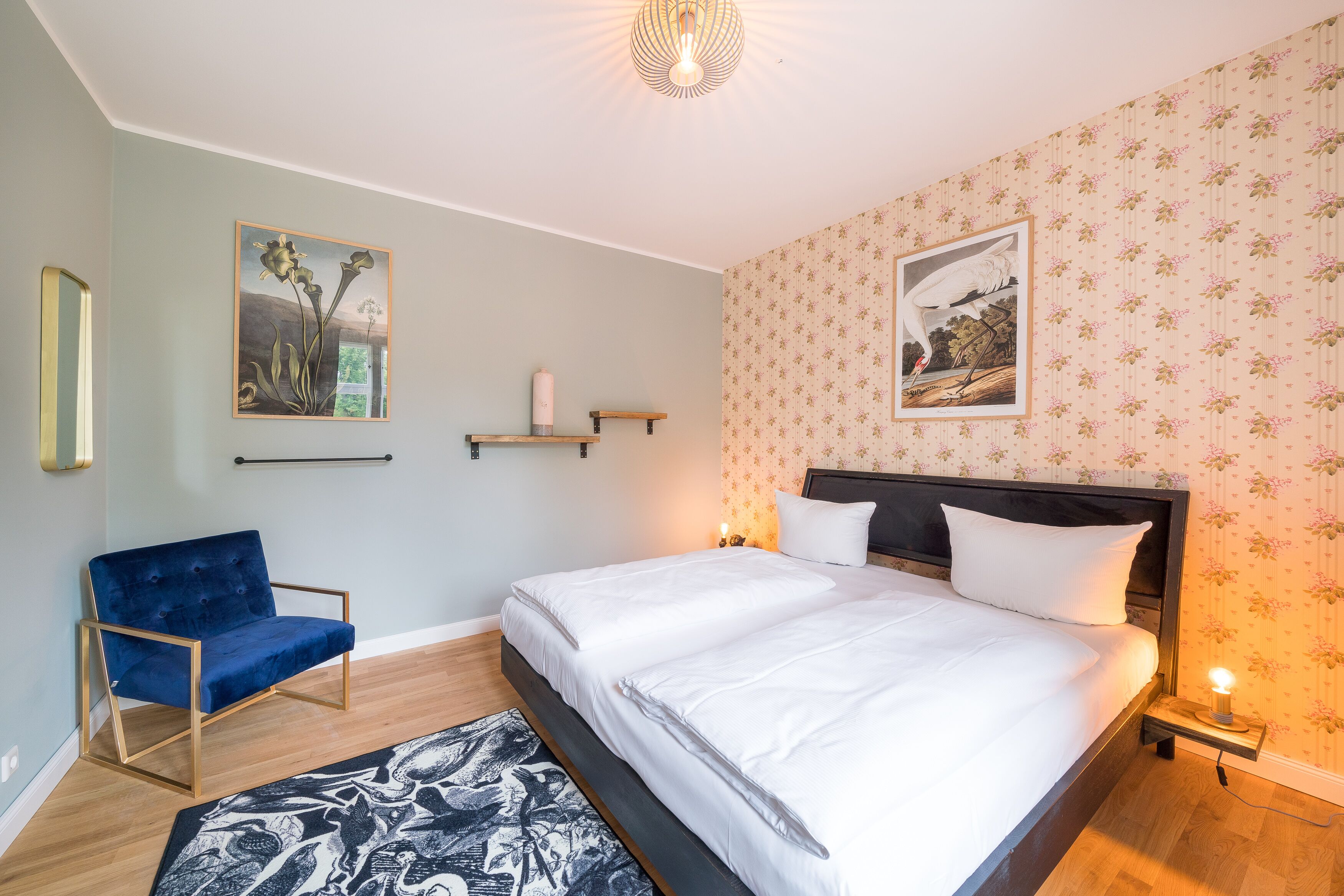 A bedroom with a bed, a blue chair, a nightstand, and two wall-mounted shelves.