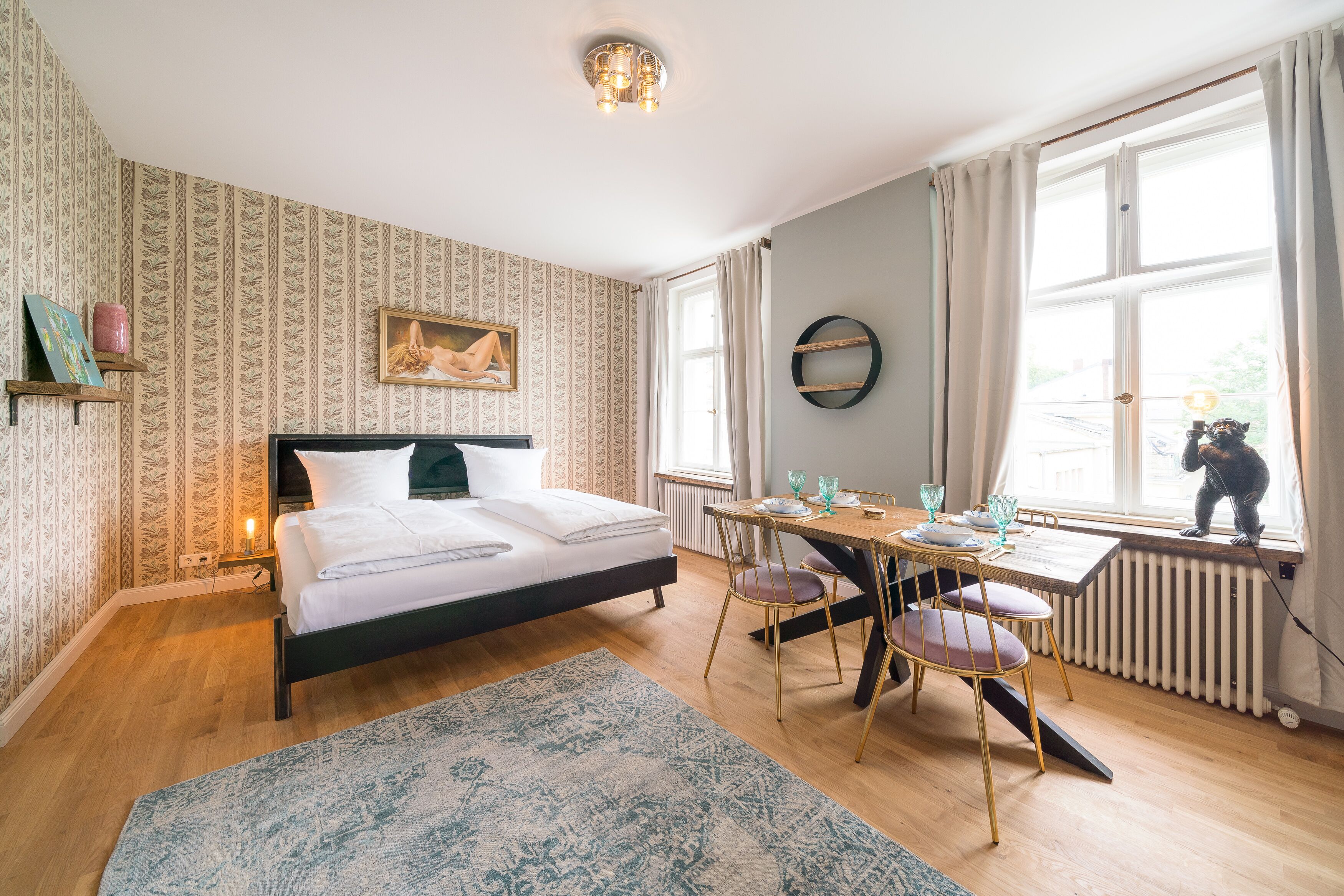 A bedroom with a bed, a dining table with chairs, a window with curtains, and a radiator.