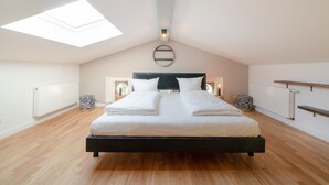 Un dormitorio amplio con tragaluces, una cama grande, mesitas de noche y un estante empotrado.