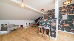 Un loft moderno con piso de madera, un sofá gris, una zona de comedor con sillas rojas y un vibrante mural con motivos de peces.