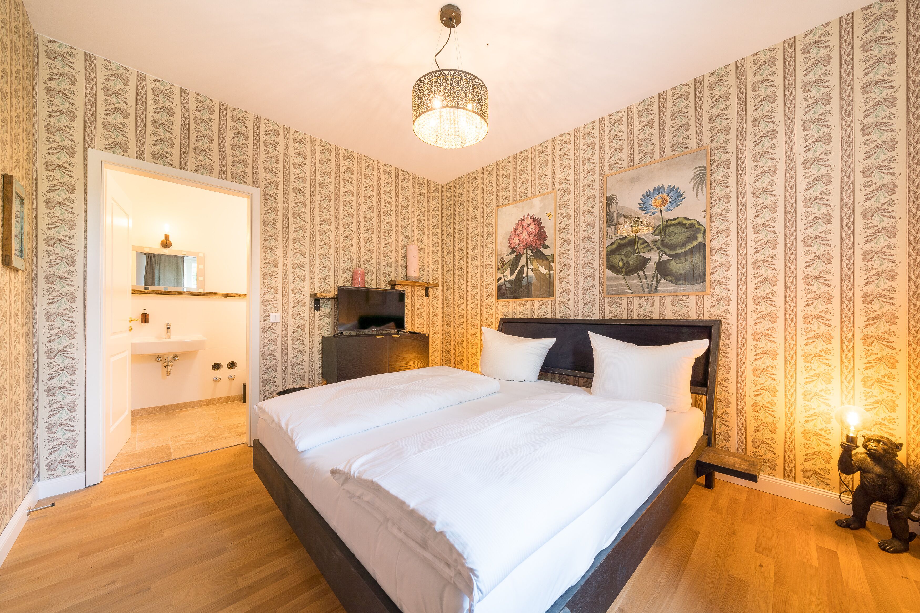 Ein Schlafzimmer mit einem großen Bett, einem Nachttisch, einem Spiegel, einem an der Wand montierten Fernseher und einem kleinen Tisch mit einer Lampe.