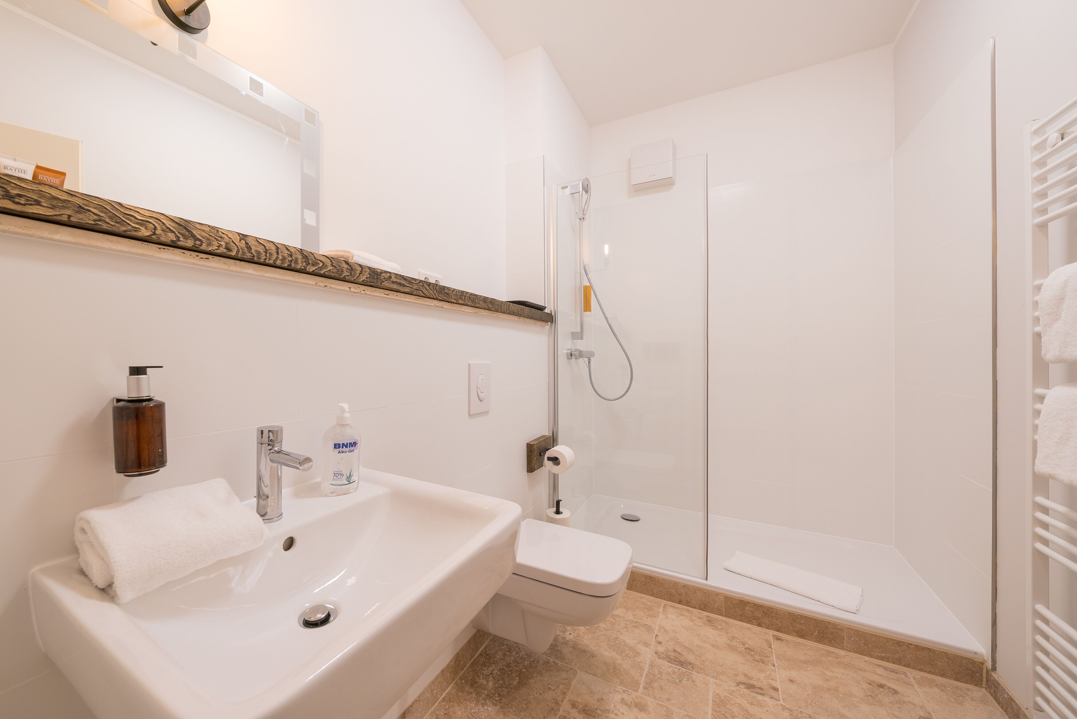 A modern bathroom with a white sink, a glass shower enclosure, and a wooden shelf above the sink.