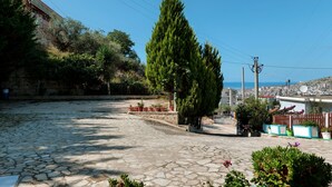 A cobblestone courtyard with potted plants, a tall evergreen tree, and a stone wall. - Remarkable 2-bed Apartment in Sarandë (Sarandë)