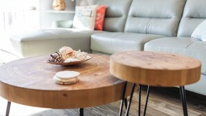 A round wooden coffee table with a bowl and a plate, a matching stool, and a grey sofa with cushions in a modern living room.