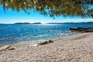 A pebbled beach with clear blue water, a distant island, and a rocky outcrop. - Holiday Home Lido (Orebic)