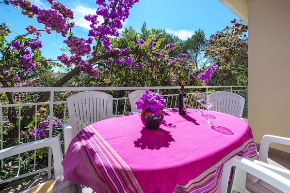 An outdoor balcony with a round table covered in a pink tablecloth, white chairs, and a vase of purple flowers. - Holiday Home Lido (Orebic)