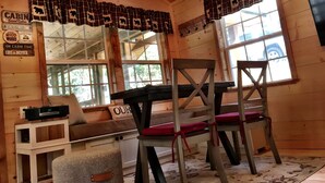 Ein Blockhaus-Interieur mit Holzausstattung, einer Bank mit Kissen, zwei Stühlen, einem Tisch und einem Fenster mit Blick nach draußen.