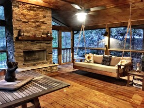 Interior acogedor de una cabaña con chimenea de piedra, una mecedora de madera y una estatua de perro.