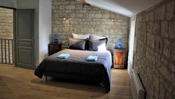 Une chambre avec un mur en pierre, un lit avec des oreillers, une table de chevet avec une lampe et une porte.