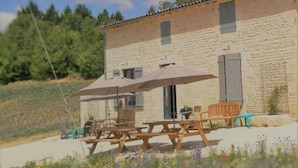 Un bâtiment en pierre avec une table et des chaises en bois, une table de pique-nique et un espace abrité.