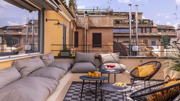 Una terraza en la azotea con un sofá, una pequeña mesa con frutas y vasos, y una silla.