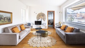 Un salón amplio con un sofá gris, un televisor y un ventanal grande.