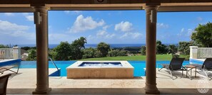 A pool area with a hot tub, lounge chairs, and a view of the ocean.