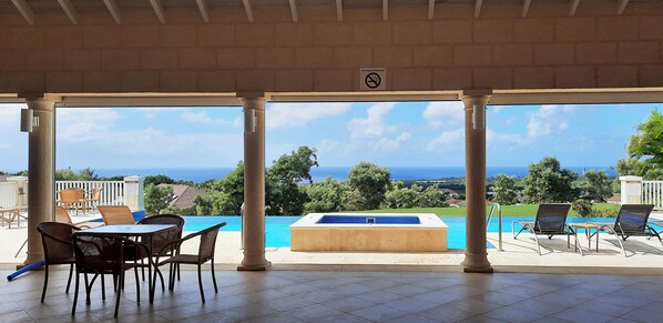 A covered outdoor area with a pool, lounge chairs, and a table.