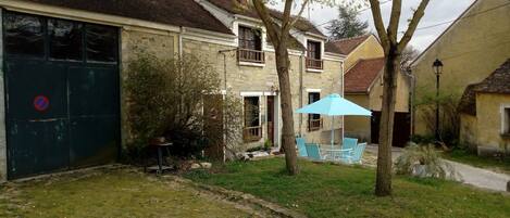 Un quartier résidentiel avec une maison dotée d’un garage, d’un petit jardin agrémenté d’un parasol bleu et d’un arbre.
