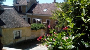 Ein Innenhof mit einem Pflasterweg, einem kleinen Fenster und einem Blumentopf mit roten Blüten.