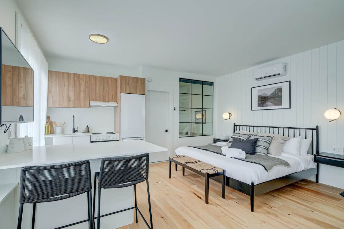 A modern, compact bedroom with a bed, bedside tables, and a large window.