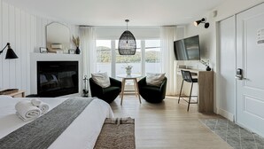 Een hotelkamer met een bed, een televisie, een bureau, twee stoelen, een open haard en uitzicht op het omliggende landschap.