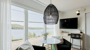 Een moderne woonkamer met een groot raam, een ronde tafel, een bank, een fauteuil en een televisie.