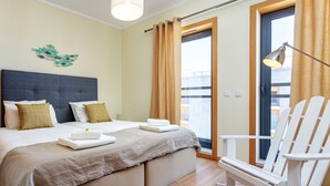 A hotel room with a large bed, two pillows, a bedside table, a chair, and a window with curtains. - Luxury 2-Bedroom Apartment with RiaView & Rooftop Pool, Village Marina, Olhão (Olhão)