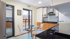 A modern kitchen with a glass table, wooden stools, and a black countertop. - Luxury 2-Bedroom Apartment with RiaView & Rooftop Pool, Village Marina, Olhão (Olhão)