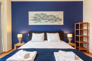 Ein Hotelzimmer mit einem großen Bett, zwei Nachttischen mit Lampen, einem Holzregal und einem Wandbild mit Fischen.