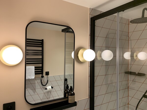 Un baño con un espejo grande, focos redondos en la pared, un perchero para toallas y una cabina de ducha de vidrio.
