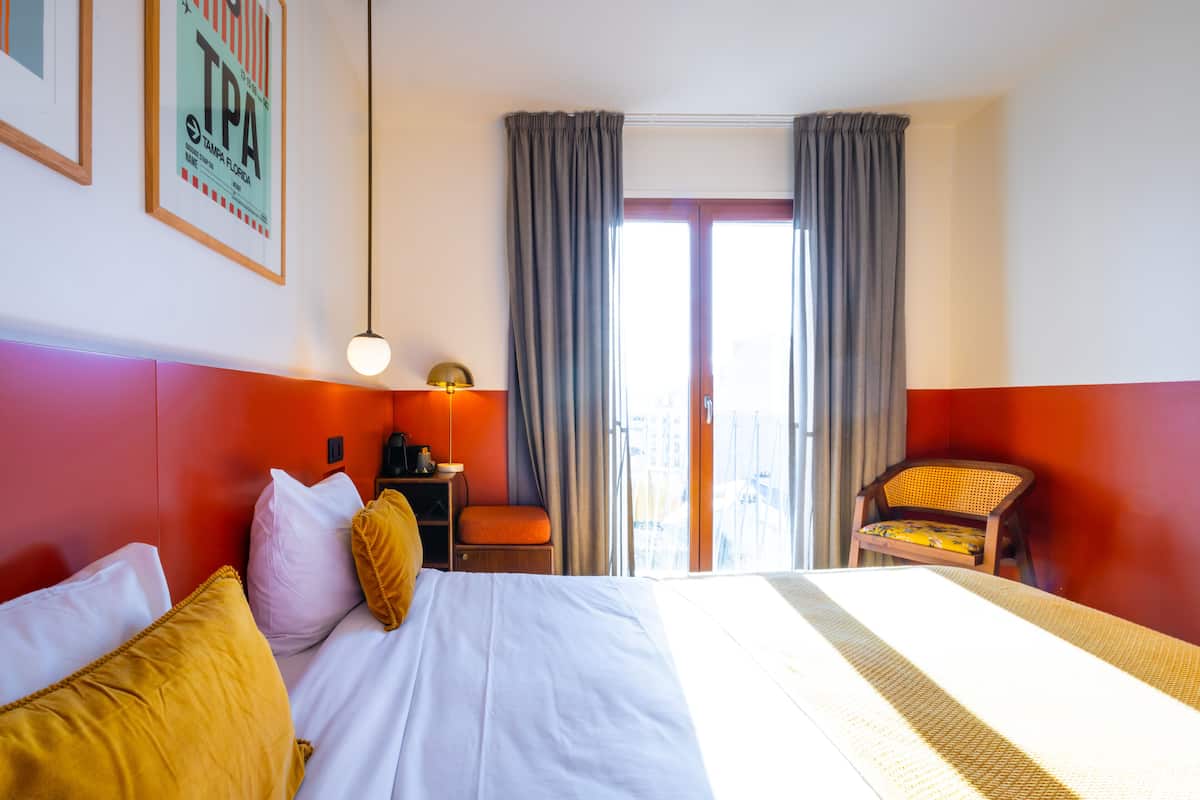 A hotel room with a bed, a chair, a desk, and a window with curtains.