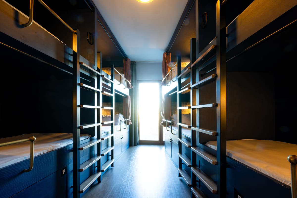 A narrow corridor with bunk beds on either side, leading to a bright window.