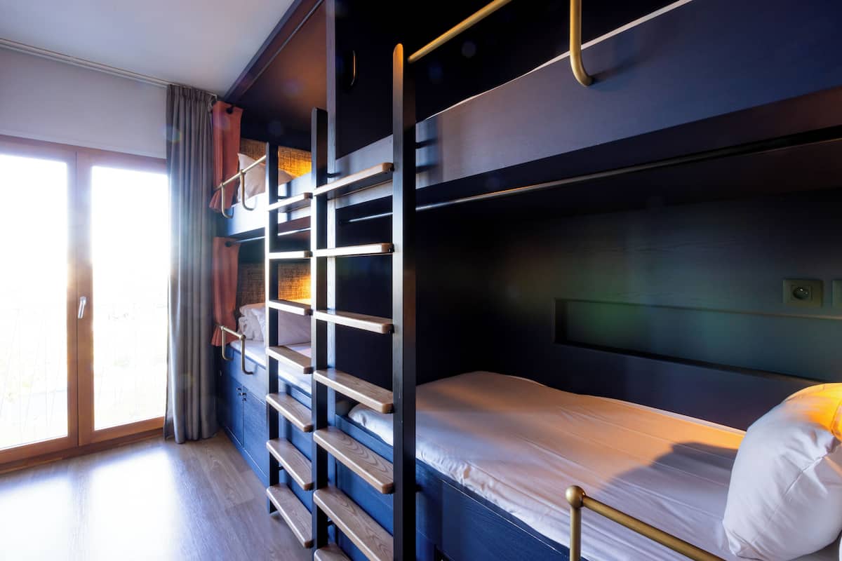 A bunk bed room with a wooden ladder, a small cabinet, and a window with curtains.