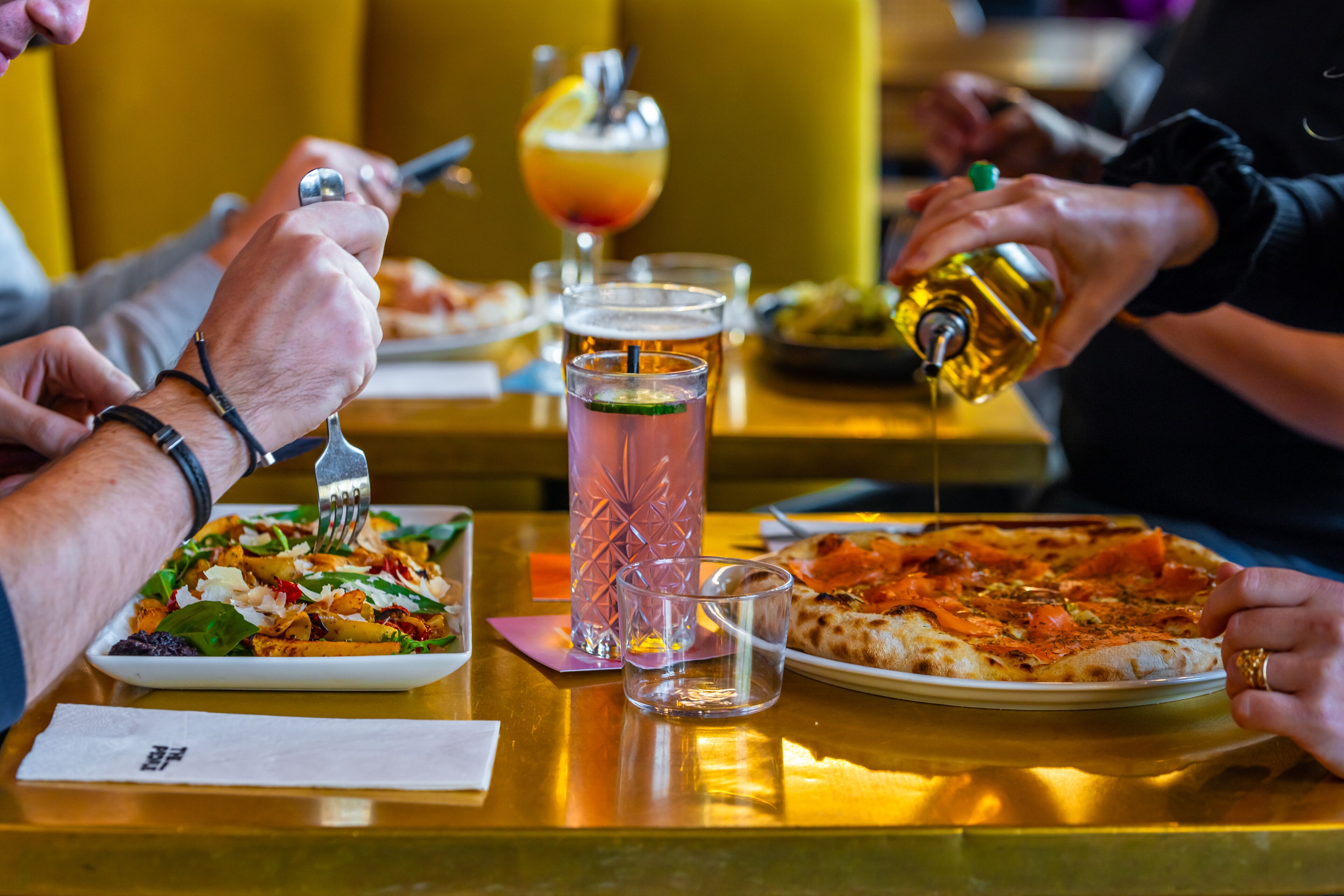 Une table à manger avec une assiette de nourriture, un verre de bière et une personne en train de verser une boisson.