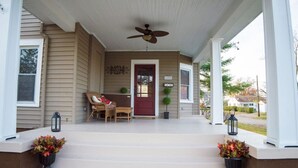 Eine überdachte Veranda mit roter Tür, einem Deckenventilator und zwei Blumentöpfen.