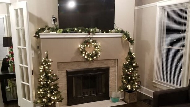 Ein Wohnzimmer mit Kamin, zwei Weihnachtsbäumen und einem flachbildfernseher über dem Kaminvorsatz.