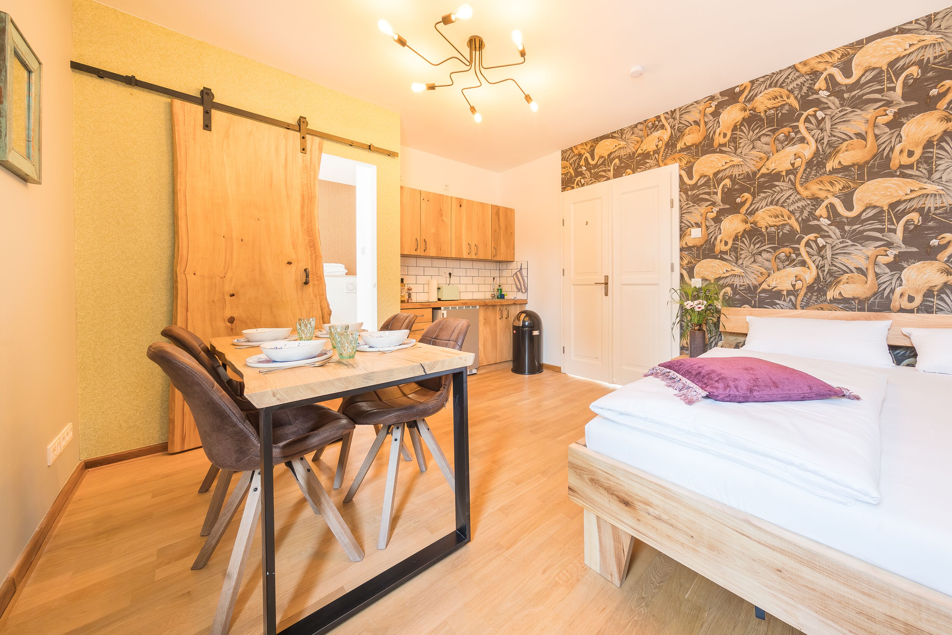 A room with a bed, a dining table with chairs, a kitchen area, and a bathroom.