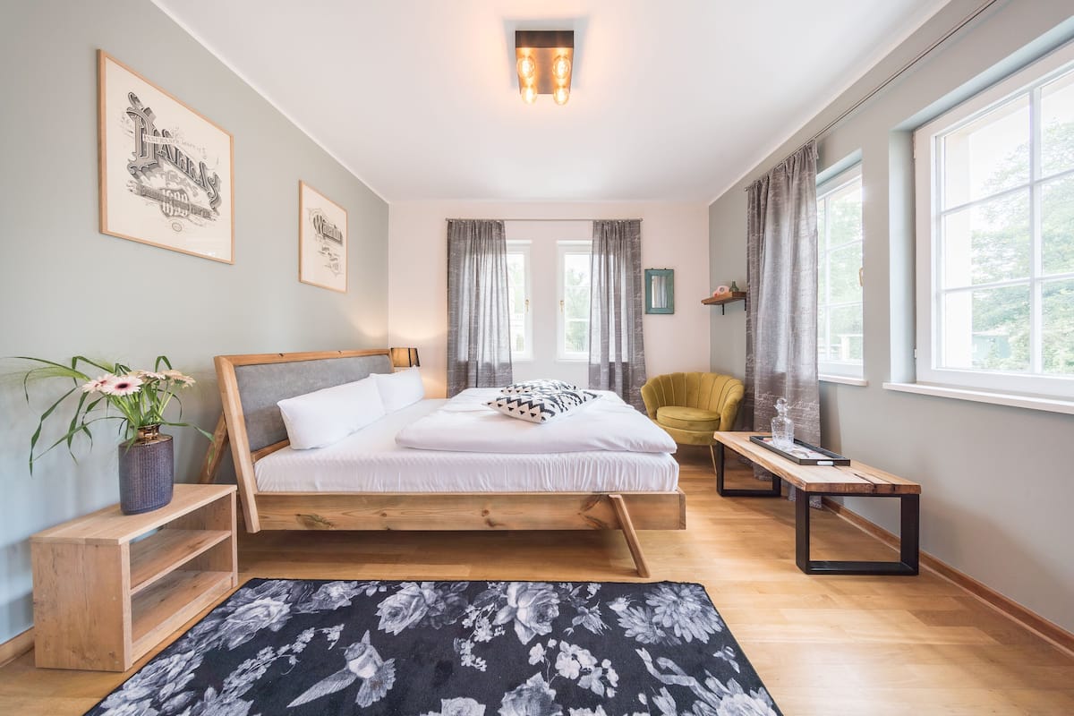 Ein Schlafzimmer mit Bett, Nachttischen, einer Bank, einer Topfpflanze und einem Fenster mit Vorhängen.